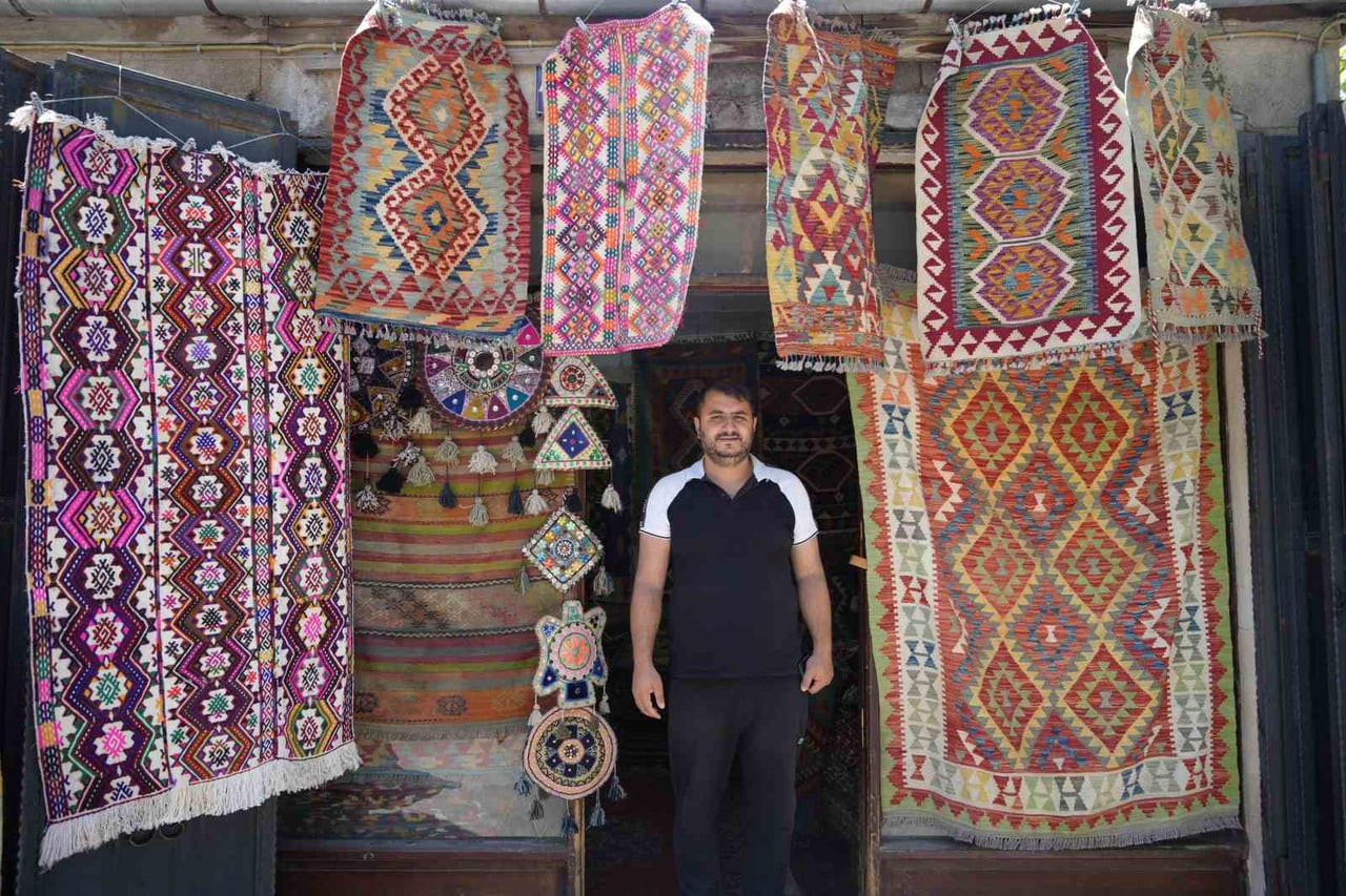 YÖRÜK KÖYLERİNDEN TOPLADIĞI HALI VE KİLİMLERİ SATARAK GEÇMİŞİ GELECEĞE TAŞIYOR